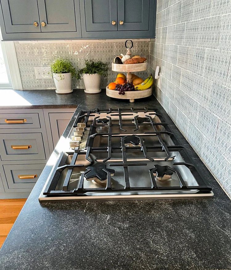 Kitchen with blue cabinets, gas stovetop, fruit stand, and patterned backsplash.