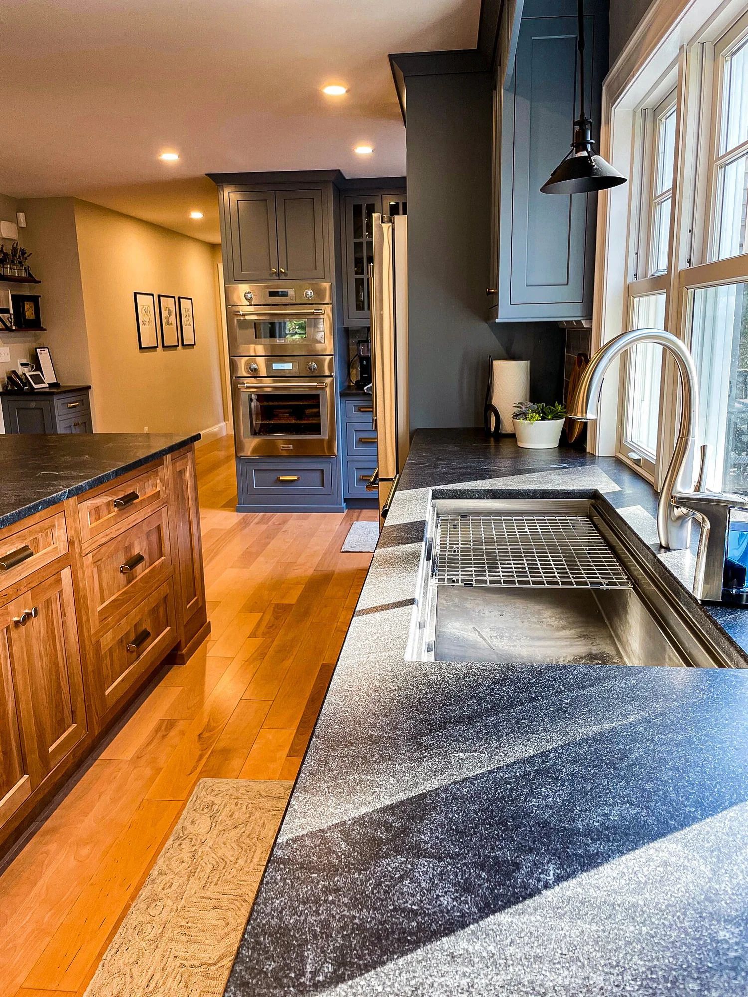 Kitchen with blue cabinets, stainless steel sink, black countertops, and wooden island.