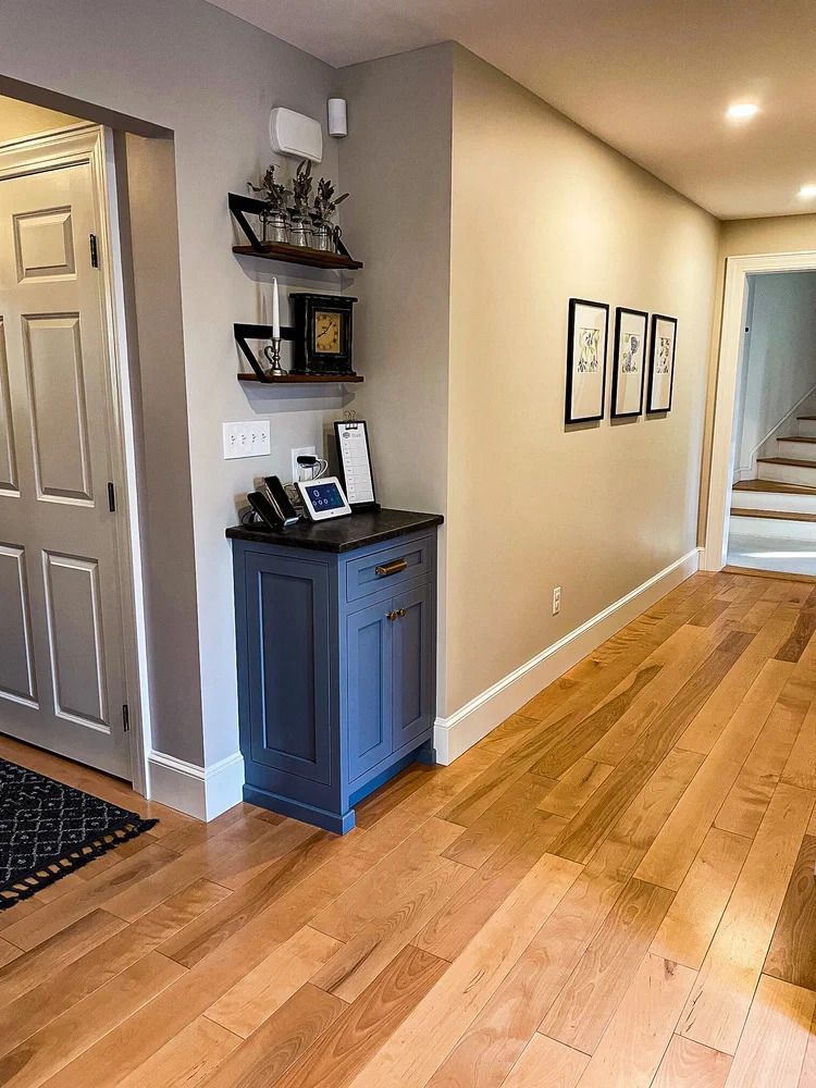 A hallway with hardwood floors, a blue cabinet, shelves, artwork, and a doorway.