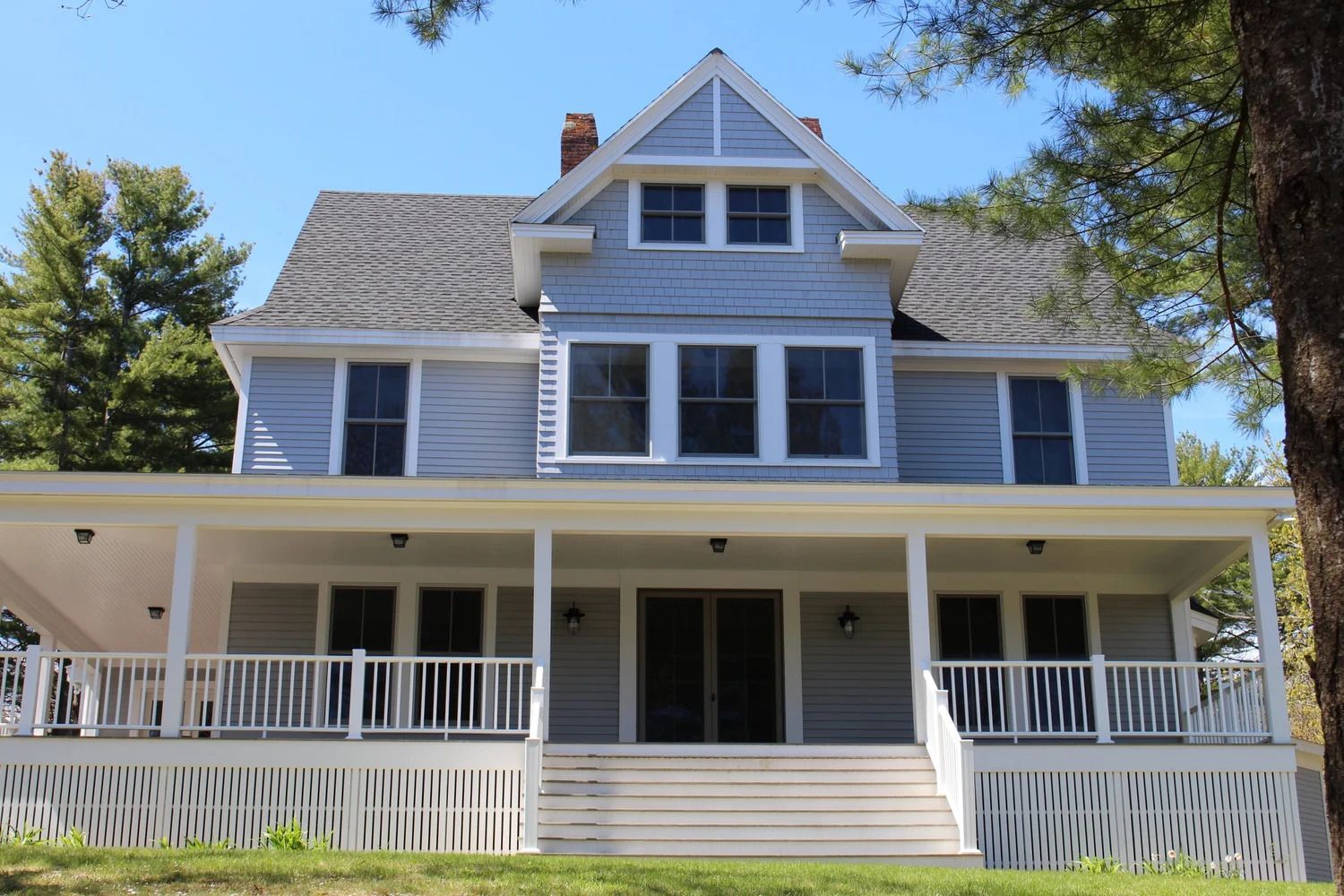 Blue two-story house with a porch and white railings under a clear sky.