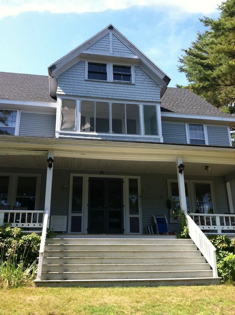 Two-story, light gray house with a porch and steps, blue accents. Sunny day.