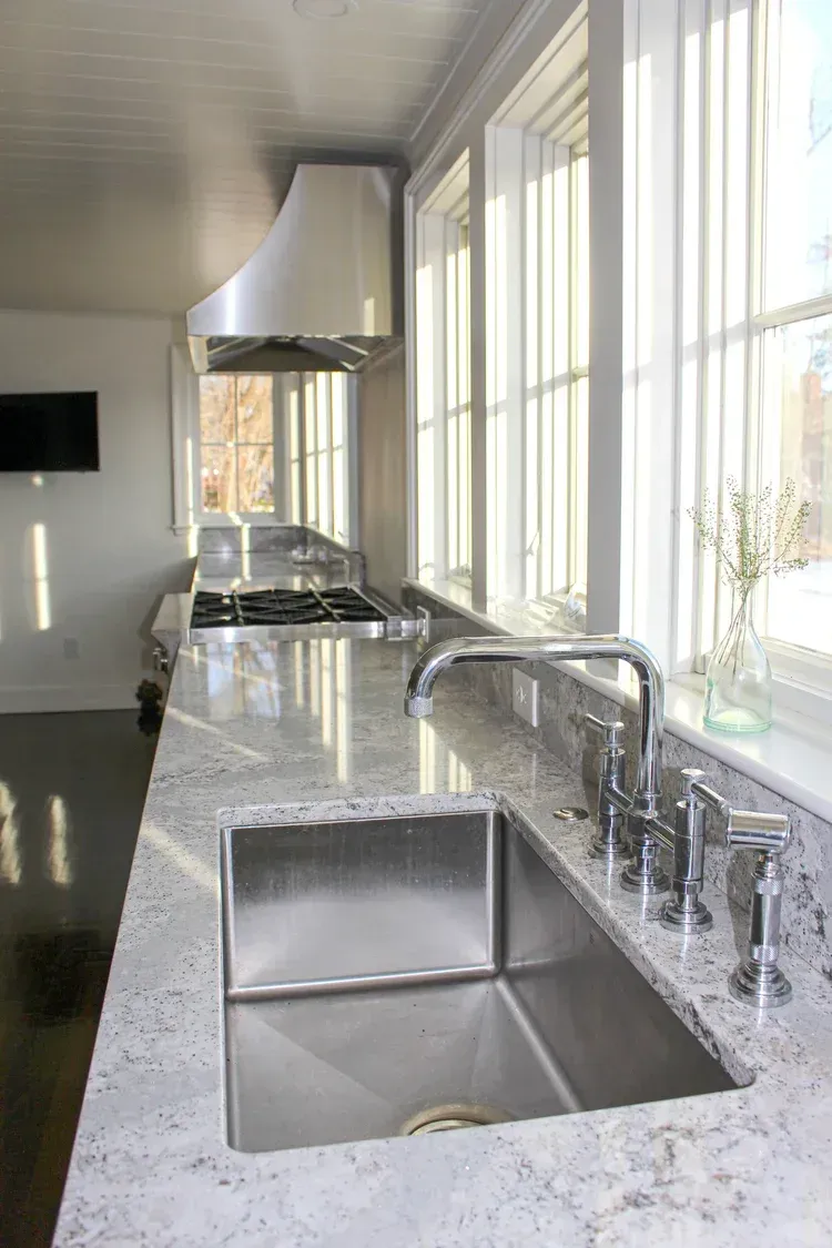 Stainless steel kitchen with granite countertop, sink, stove, range hood, and windows.