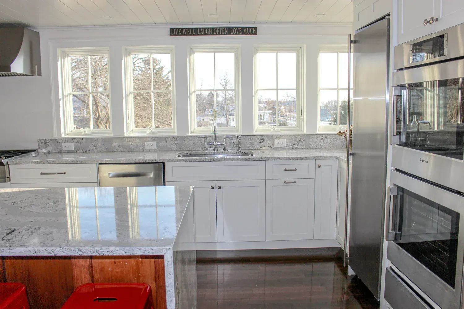 Bright white kitchen with granite countertops, stainless steel appliances, and large windows.