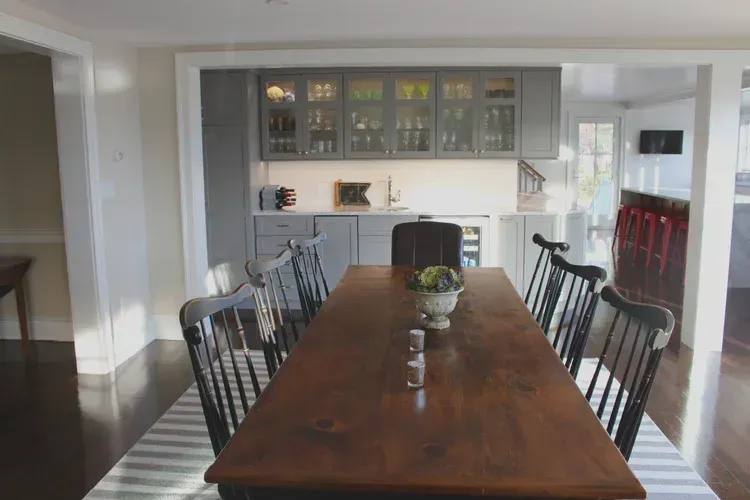 Dining room with long wooden table, six black chairs, and a grey cabinet in the background.