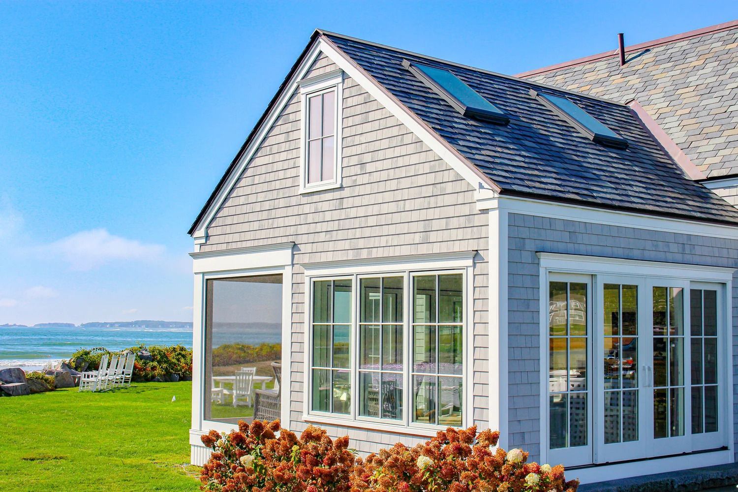Gray cottage with glass doors and windows, overlooking a beach. Blue sky.