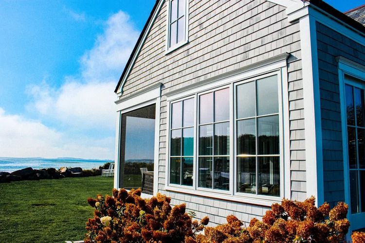 Gray shingled house with large windows, bright blue sky, and green lawn.
