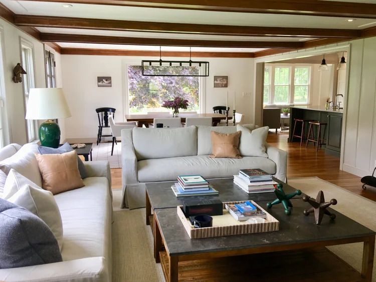 Living room with white sofas, wooden beams, a large window, and an open kitchen.