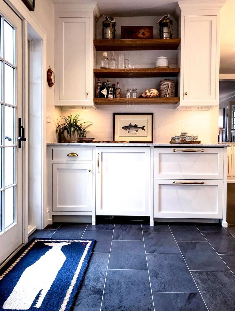 Kitchen with white cabinets, wooden shelves, and blue slate floor. Artwork of fish. Blue and white rug.