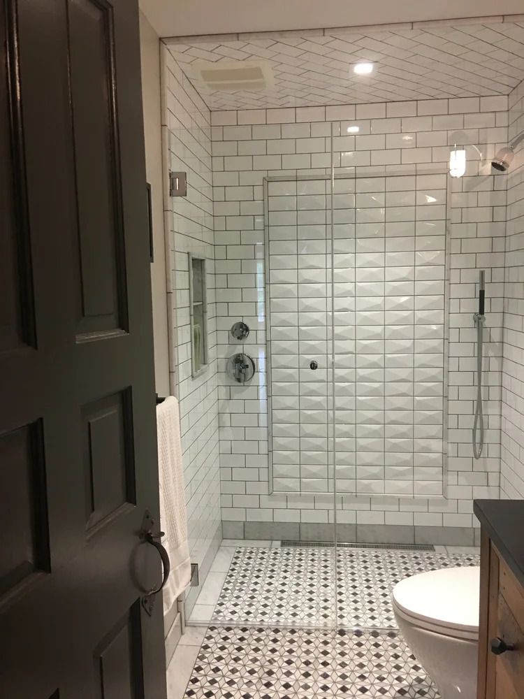 Bathroom with white subway tile shower, glass door, patterned floor, and white toilet.