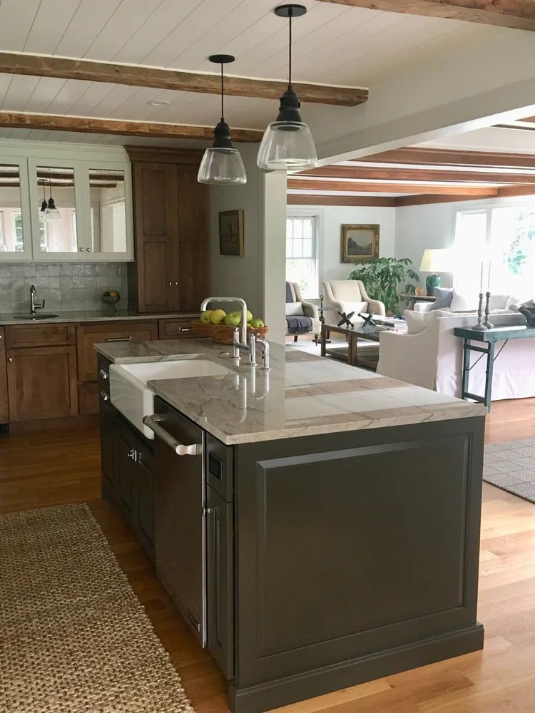 Kitchen with island, wood cabinets, sink, and pendant lights. Open to a living room with seating and windows.