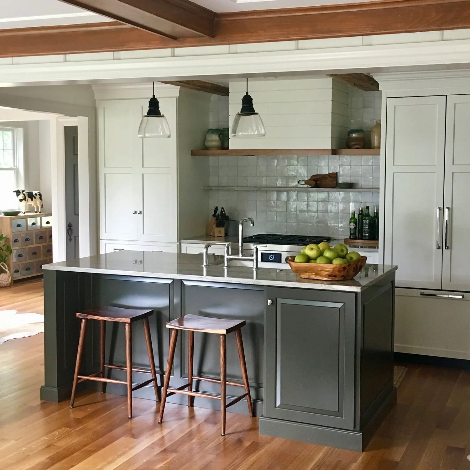 Kitchen with dark green island, white cabinets, copper stools, and wooden beams.