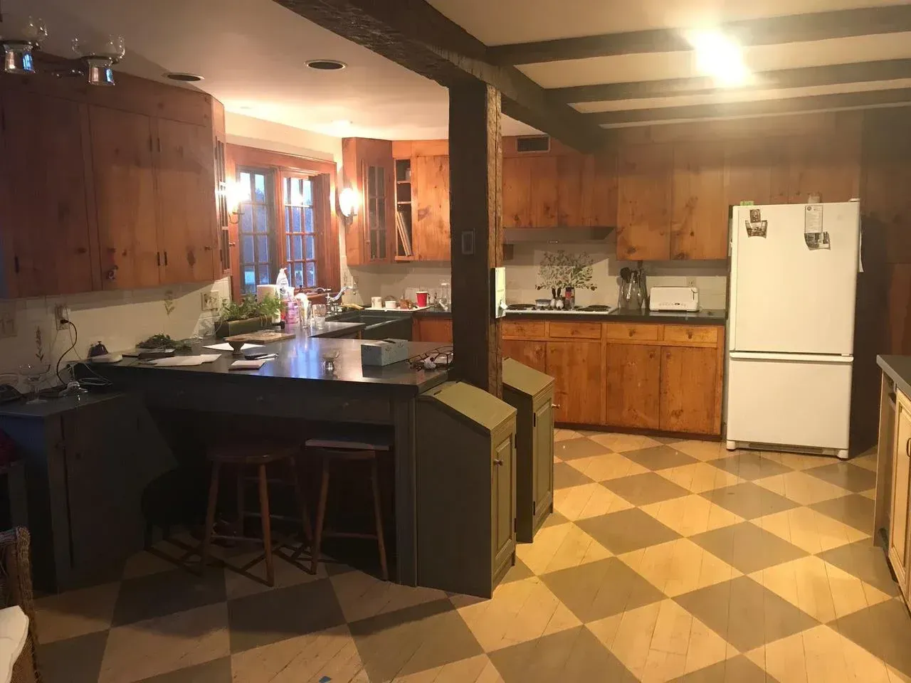 Kitchen with wood cabinets, black countertop, white refrigerator, checkered floor, and a supporting beam.