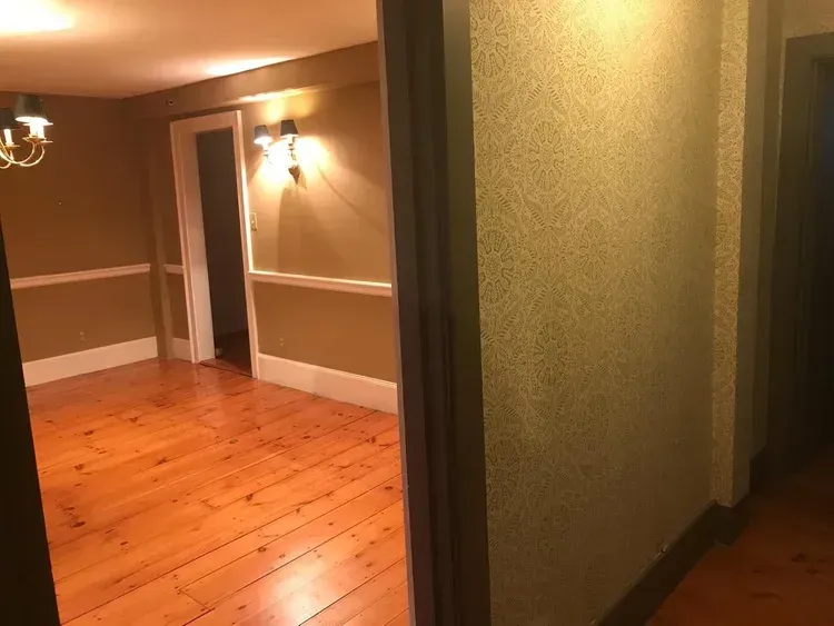 View through doorway of a room with hardwood floors and beige walls, with hallway on the right.