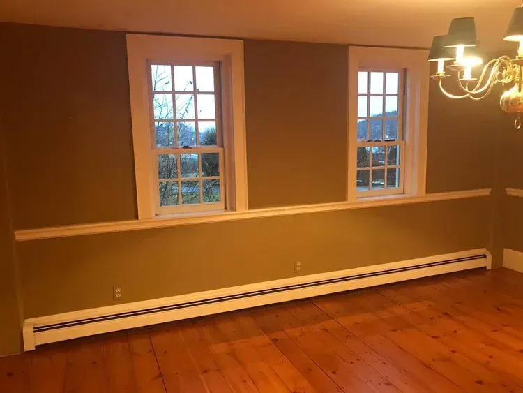 Two windows with white trim on olive green wall. Wooden floor, radiator.