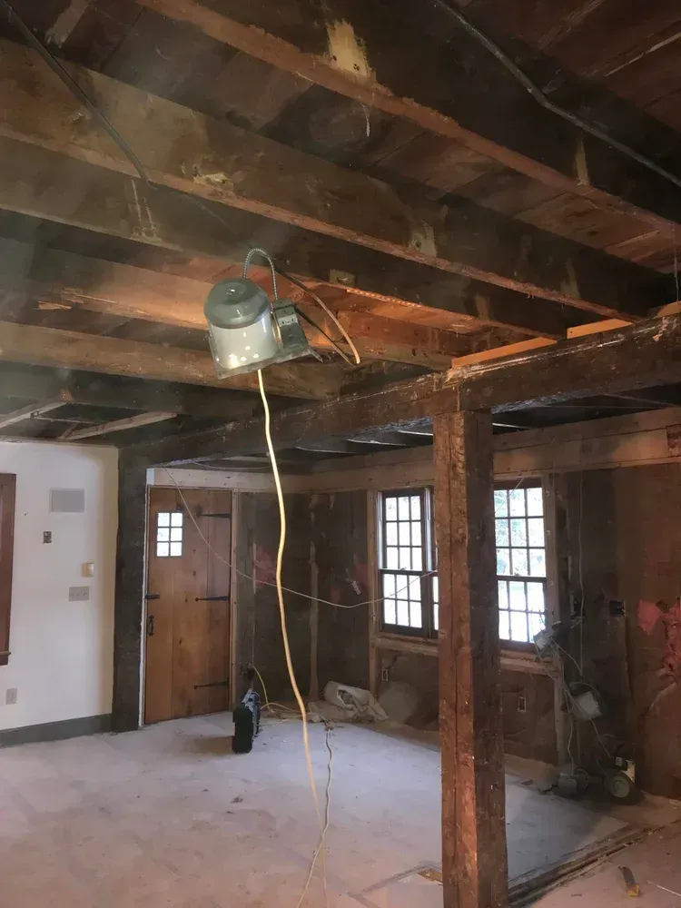 Interior of a room under construction with exposed beams, a suspended fan, and wooden doors and windows.