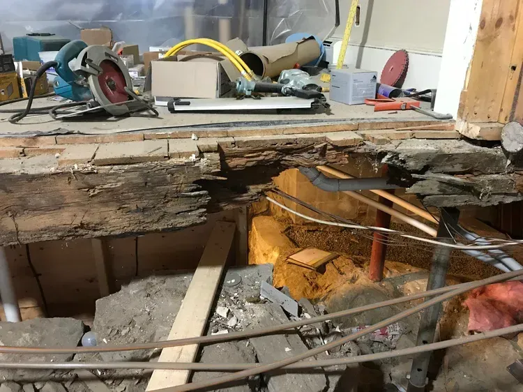 Interior shot: Damaged floor during renovation, showing exposed beams, plumbing, and construction tools.