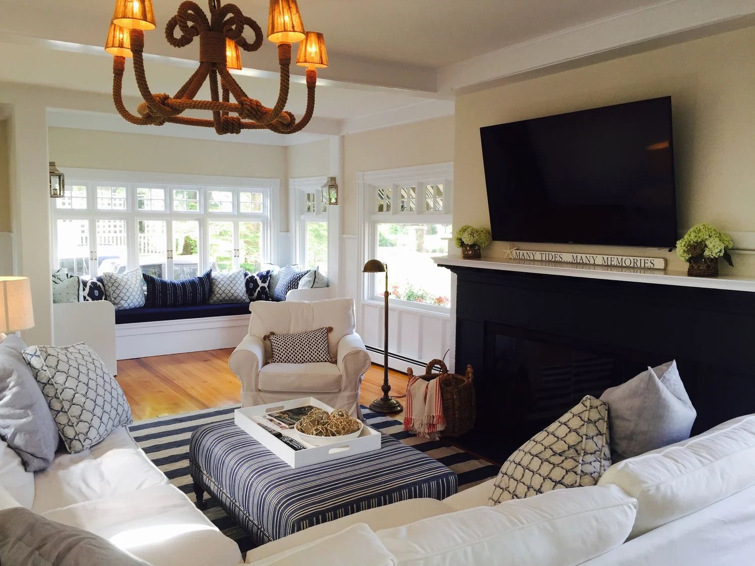 Cozy living room with white couches, striped rug, fireplace, and bay window seat filled with pillows.