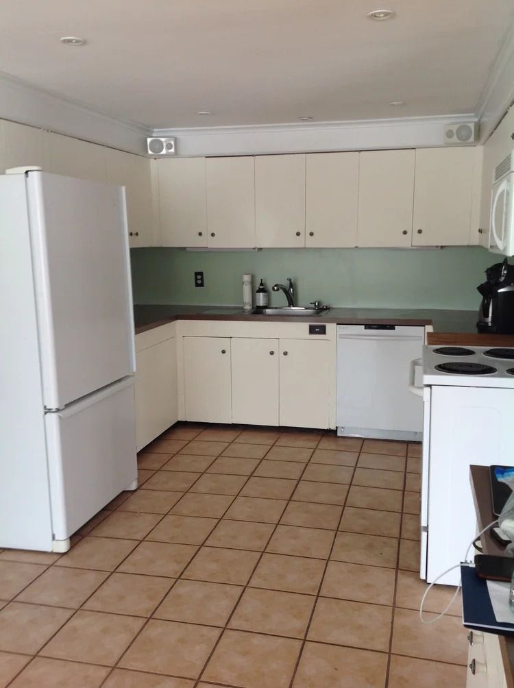 White kitchen with upper and lower cabinets, appliances, and tile floor.