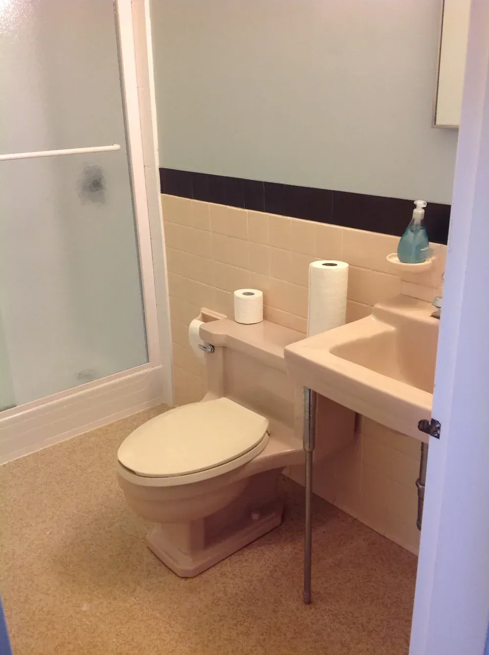 Bathroom with toilet, sink, and shower. Beige and blue walls, light floor.
