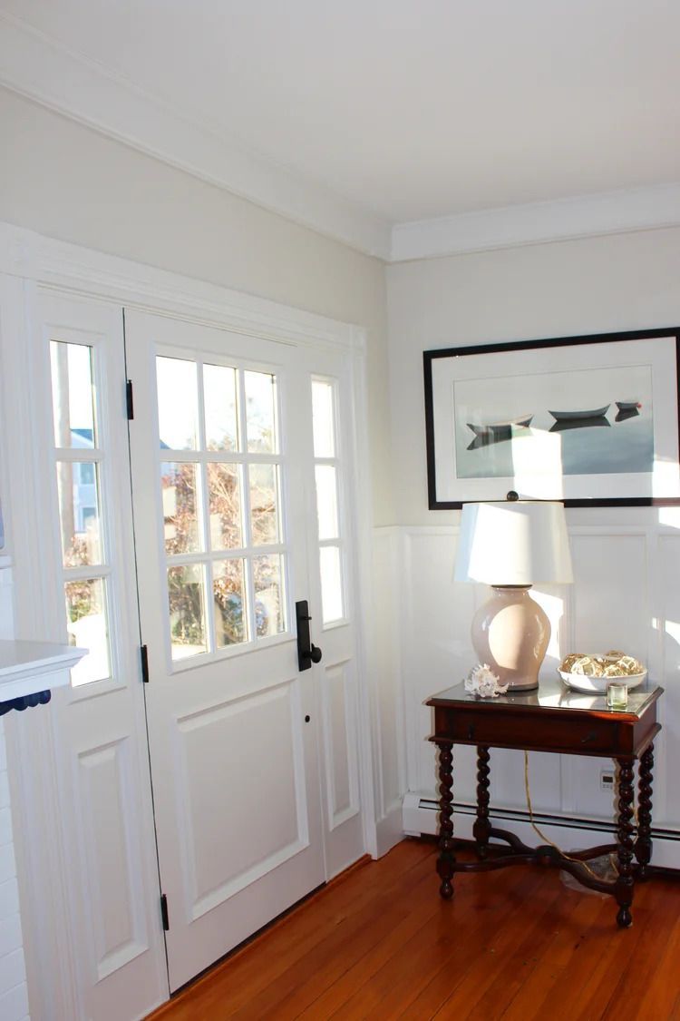 White French doors open into a bright room with a small table, lamp, and framed artwork on the wall.