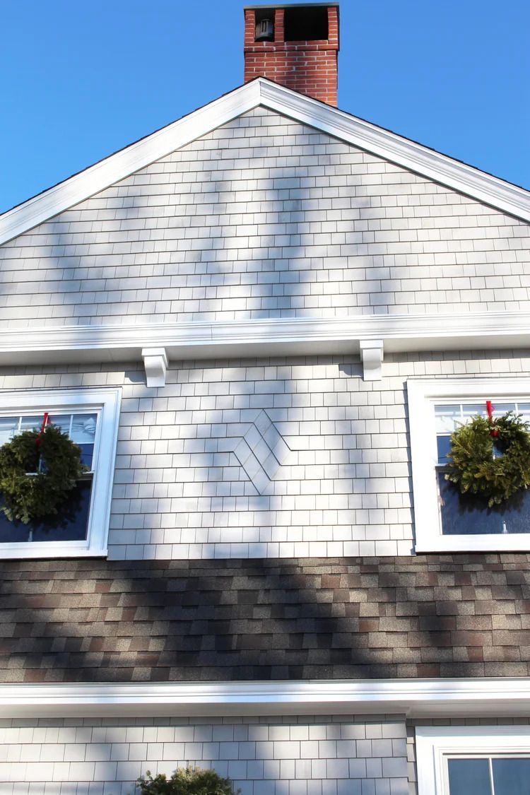 Gray house gable with two windows, each with a wreath. Red brick chimney against a blue sky.