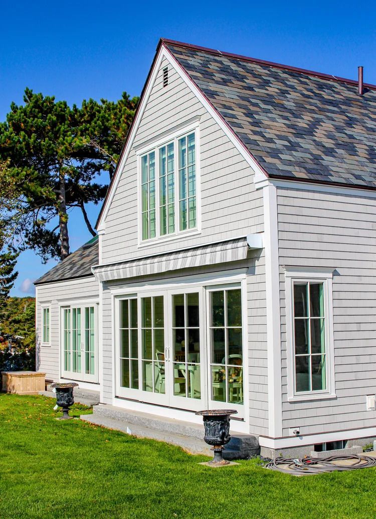 Gray house with multiple windows and a green lawn under a blue sky.