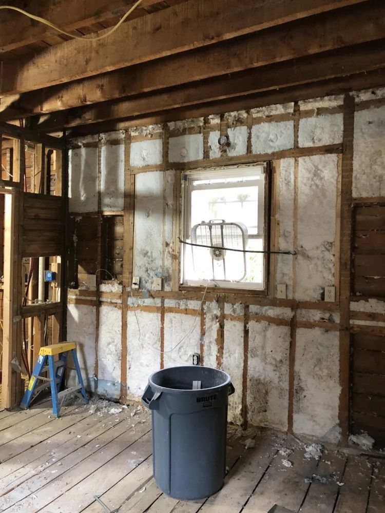 Interior room gutted during renovation, exposed wooden framing, window, trash can, ladder.
