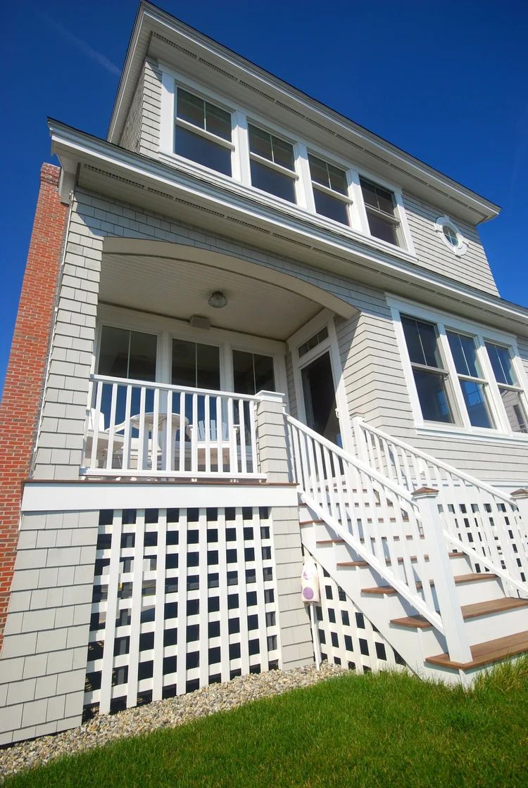 Two-story gray shingled house with white trim, red brick chimney, and open porch on a sunny day.