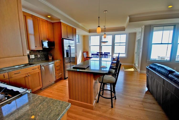 Kitchen with wooden cabinets, granite countertops, island with stools, and dining area with sunlight.