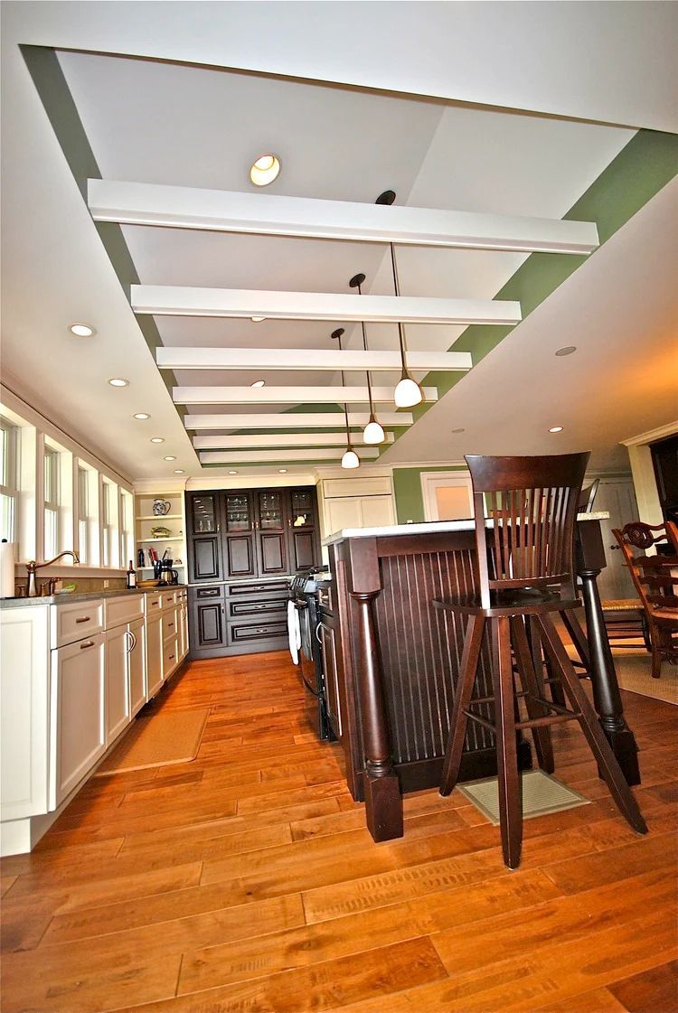Kitchen with white cabinets, dark wood island, and wooden beams on the ceiling. Hardwood floors.