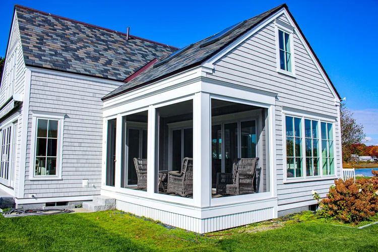 Gray cottage with a screened porch and blue sky.