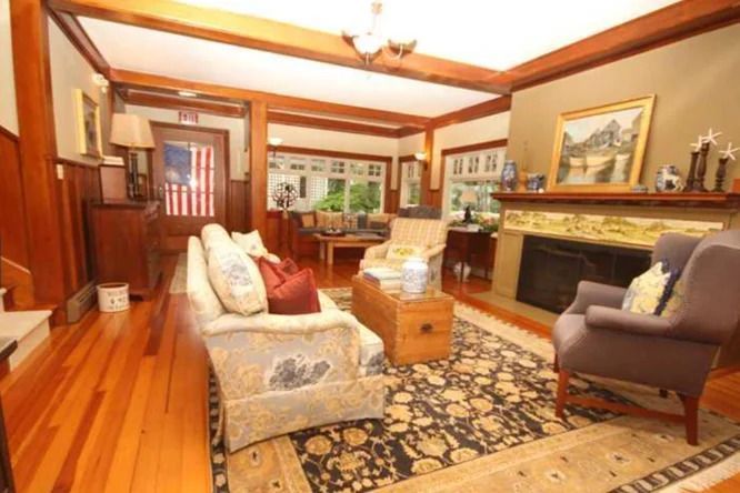 Living room with wooden beams, fireplace, patterned rug, sofa, armchair, and an American flag.