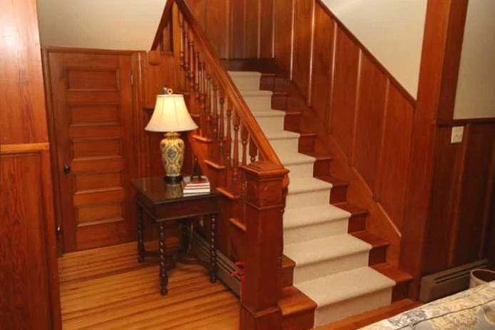 Wooden staircase with light carpeted steps, a small table with a lamp, and wooden paneling.