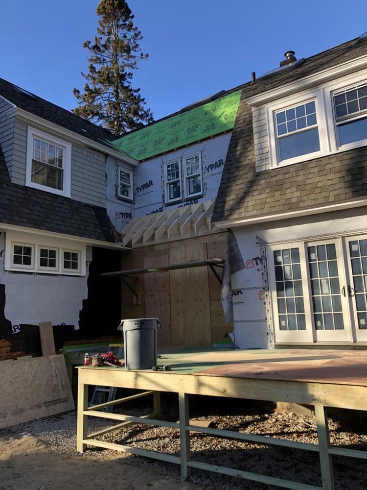 House under construction with exposed framing, tar paper, and unfinished deck.
