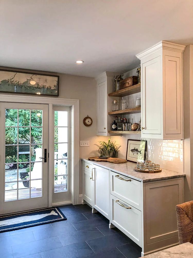 Bright white kitchen with a door to a green yard, blue rug, white cabinets, and shelves.