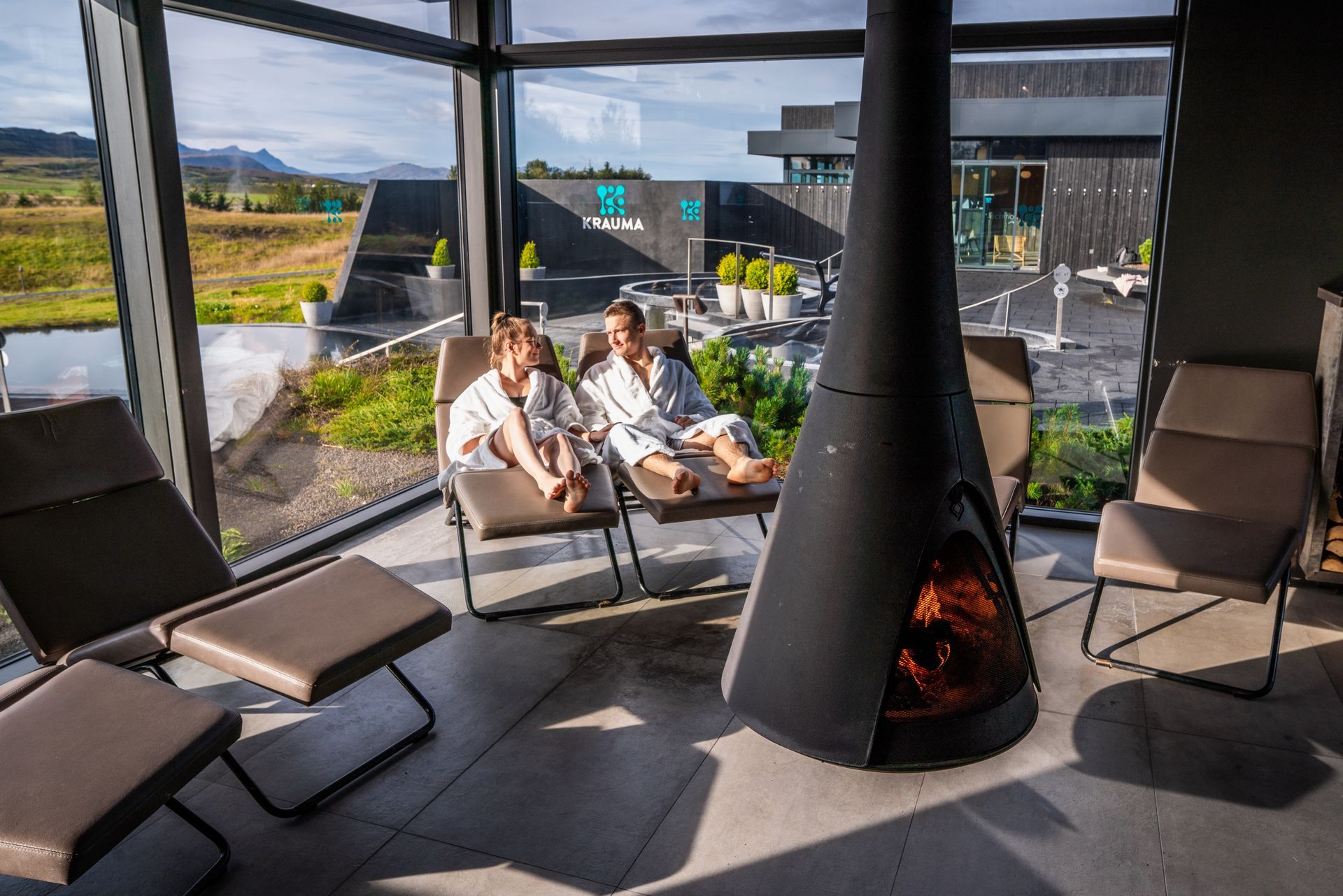 a couple sitting around the fireplace in the relaxation room at Krauma geothermal, with a beautiful large window