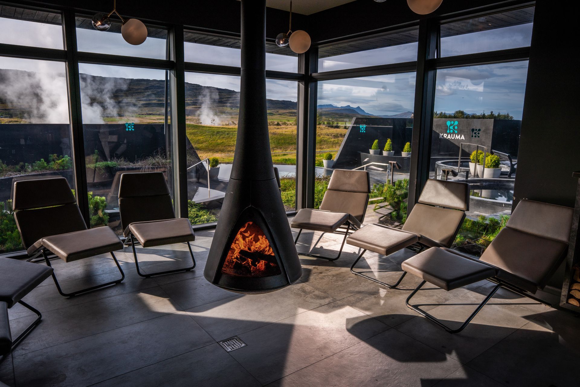a fireplace in the middle of the room with chairs around it in the relaxation room at Krauma Geothermal In Iceland,