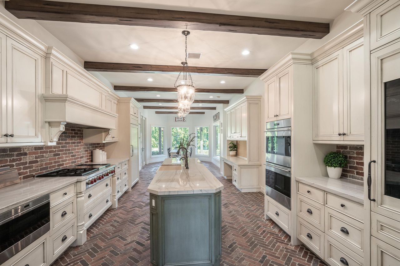 A large kitchen with white cabinets , stainless steel appliances , and a large island.