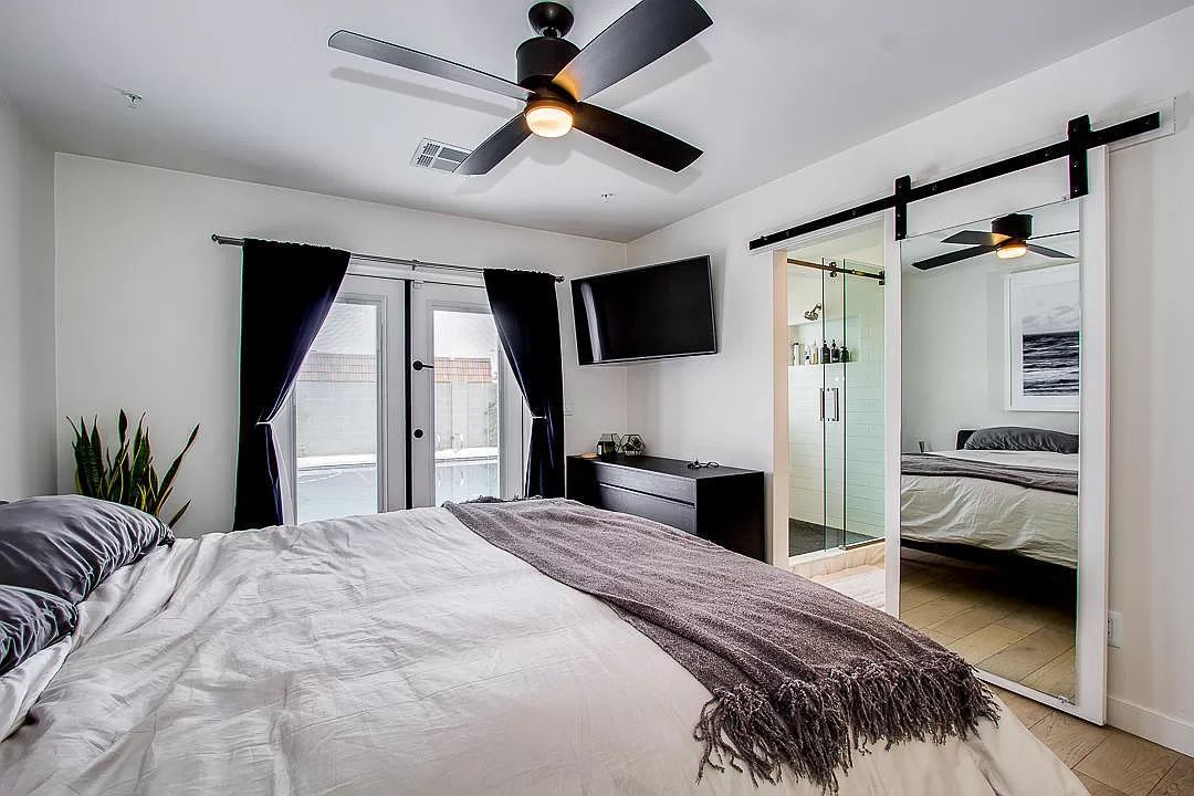 A bedroom with a bed , ceiling fan , television and sliding glass doors.