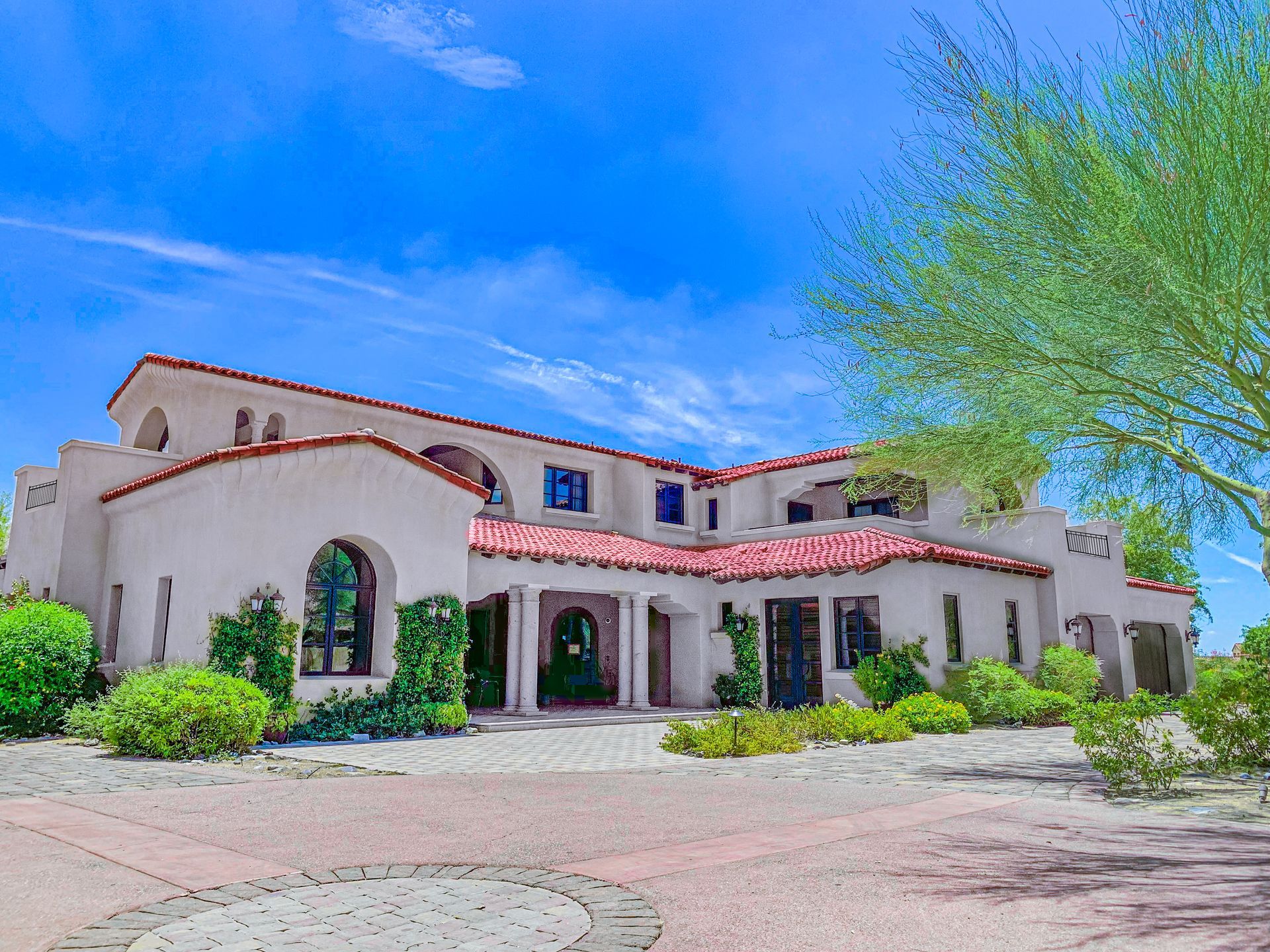 A large white house with a red tile roof is surrounded by trees and bushes.