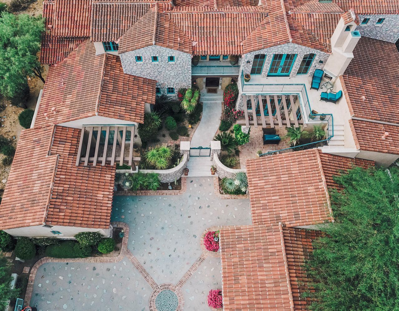 An aerial view of a large house with red tile roofs surrounded by trees.