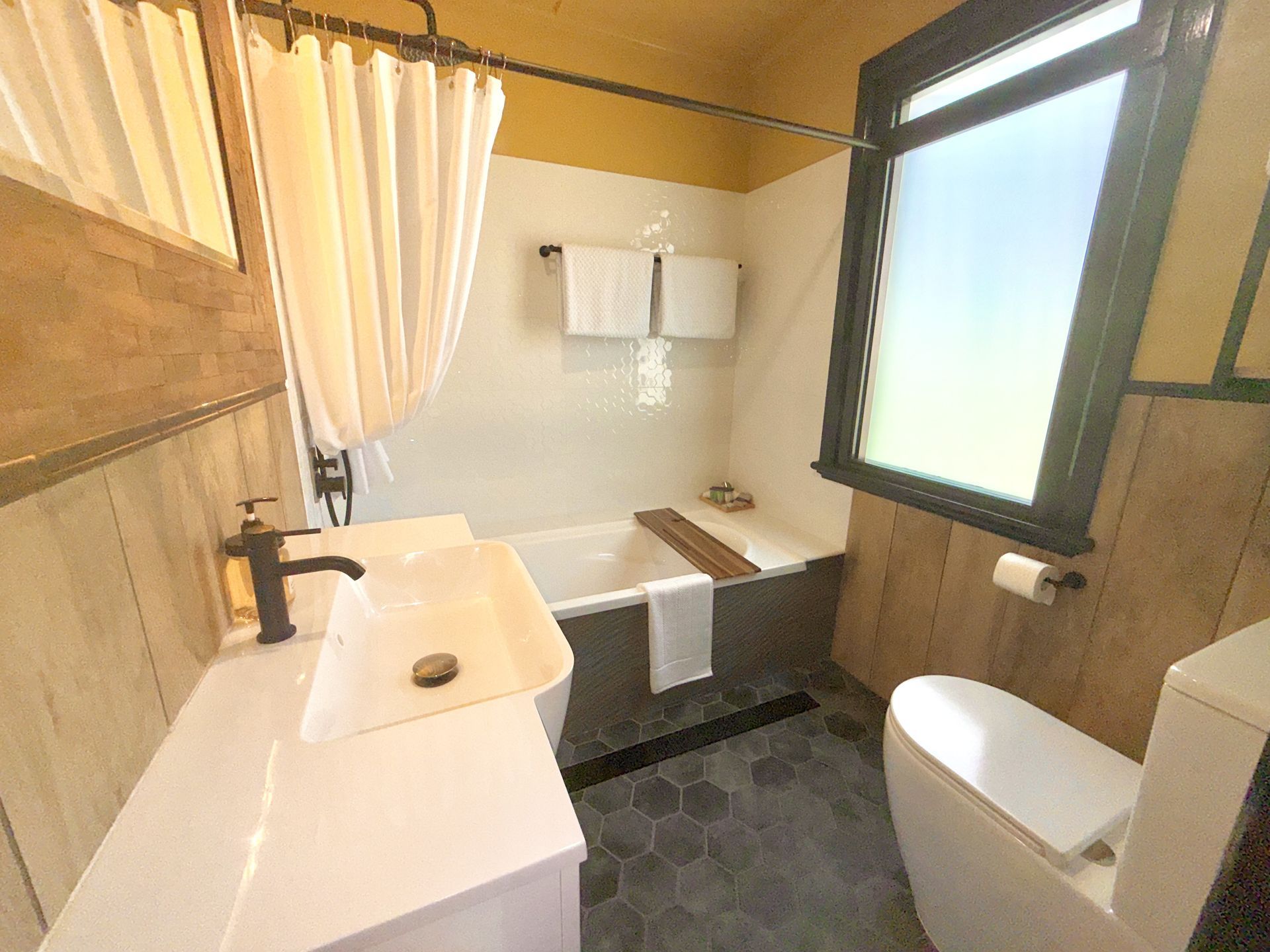A bathroom with a sink , toilet , tub and window.