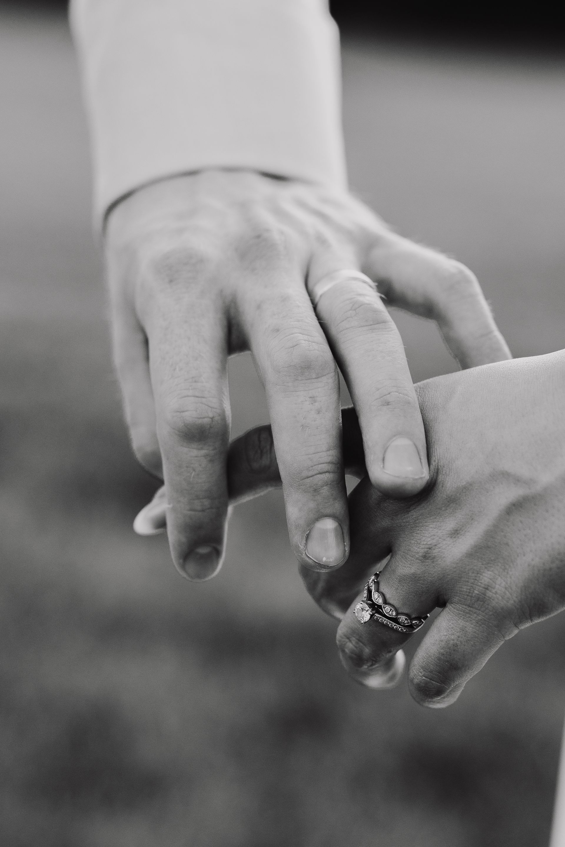 Hands holding, one wearing a wedding band, the other wearing a decorative ring.