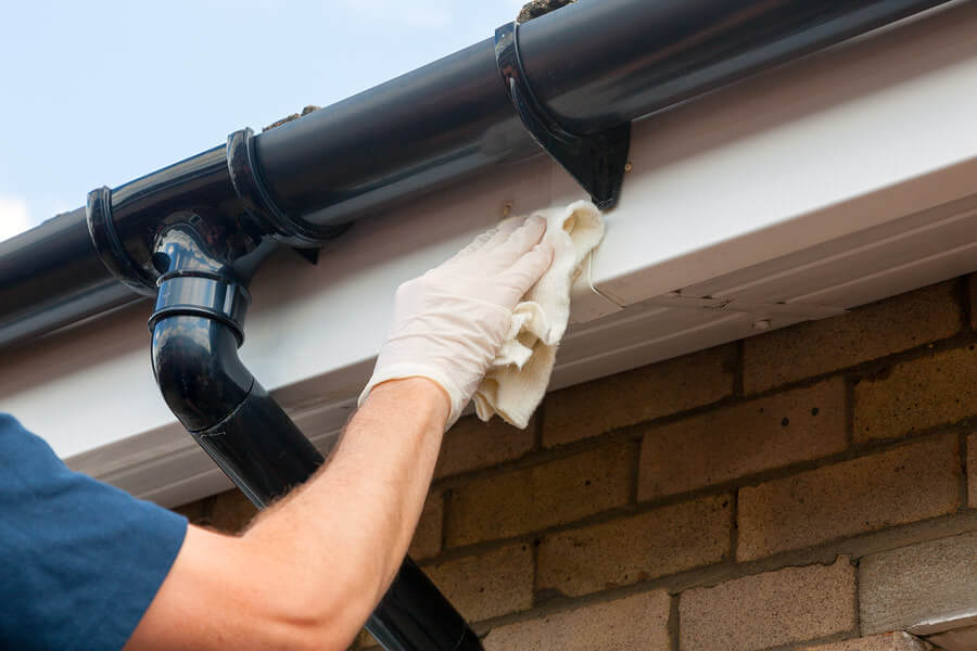 An image of a person wearing protective gloves and using a cloth to clean the gutters after they have been repaired.