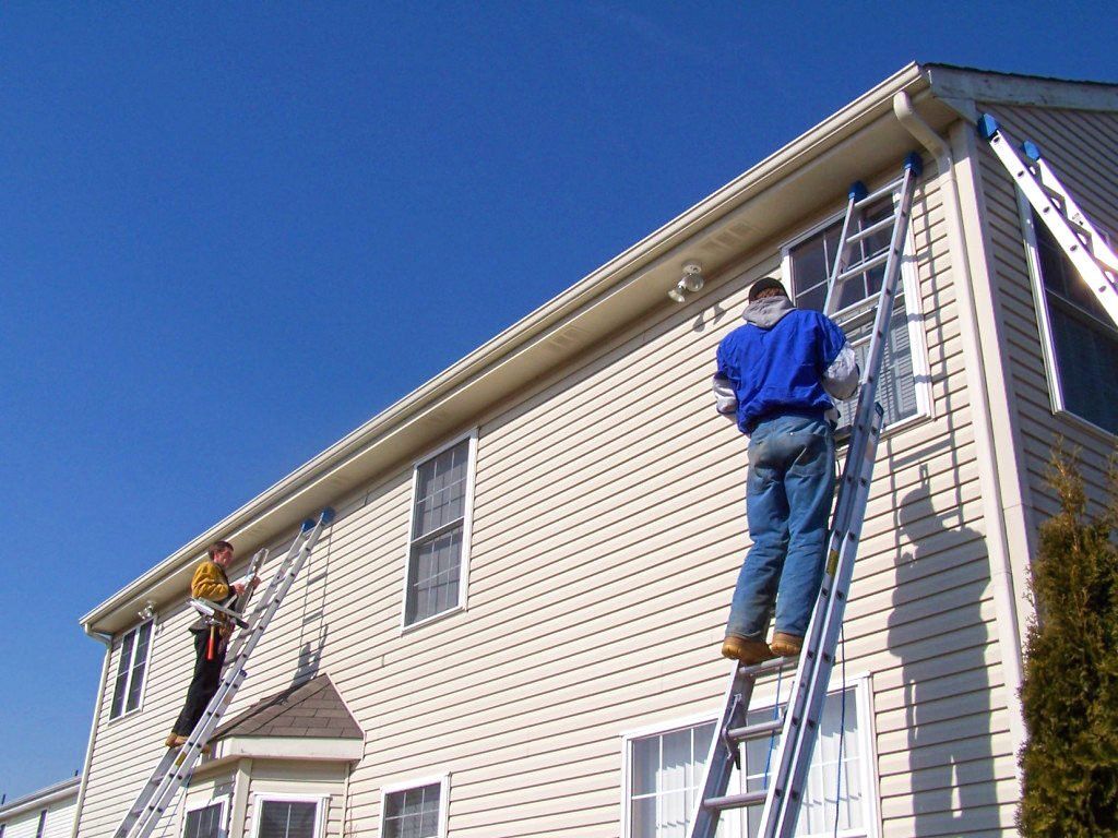 Skilled contractors repairing damaged siding on a house exterior.
