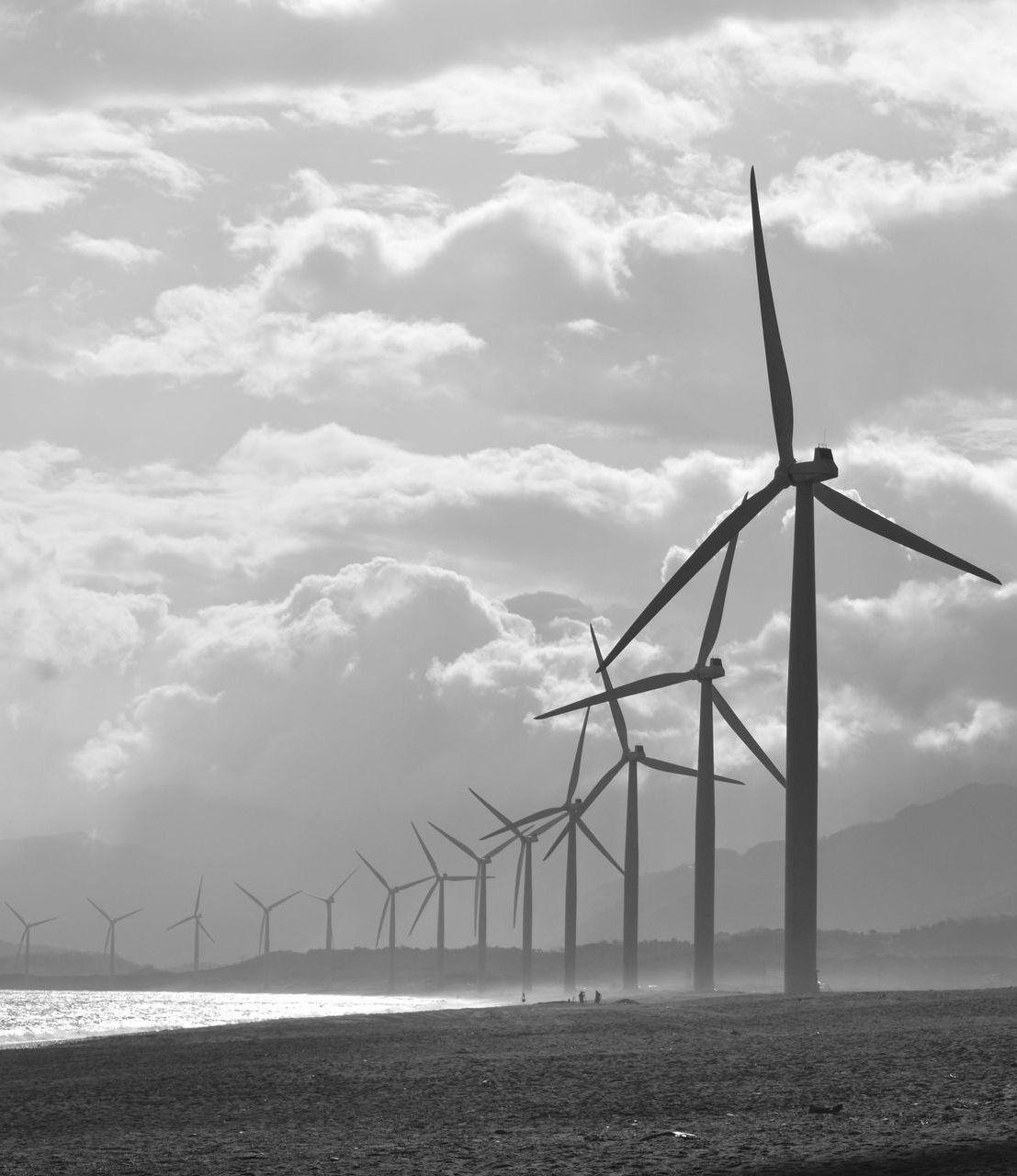Wind turbines in a field by a body of water under a cloudy sky, generating clean energy.
