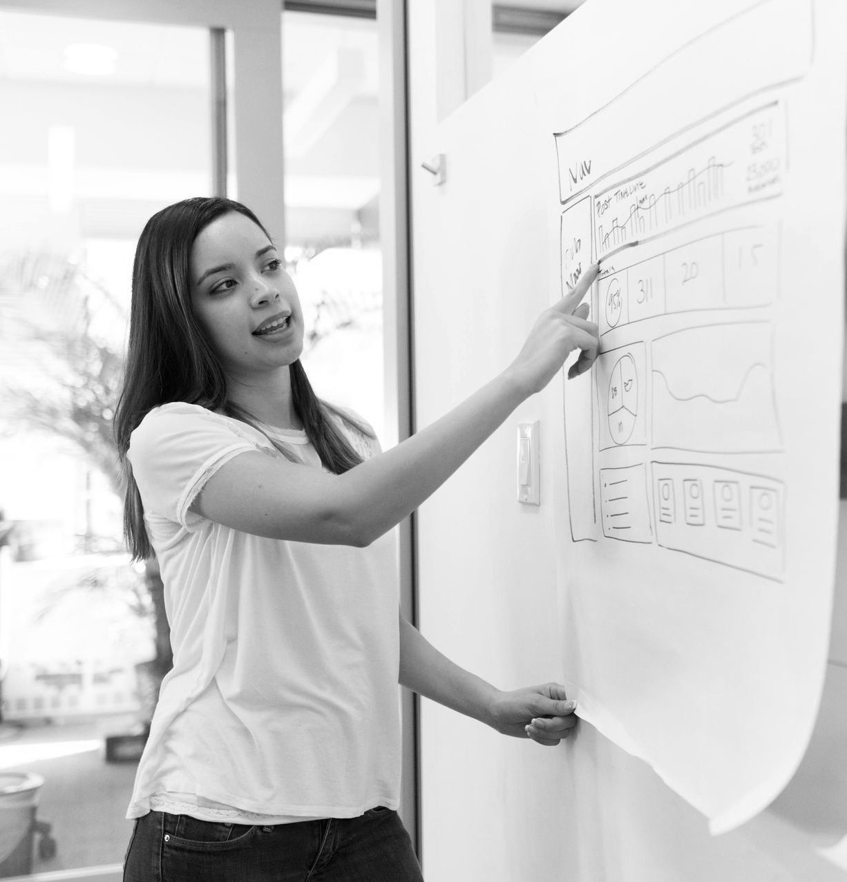 Woman points to a sketch on a whiteboard, explaining a design concept.