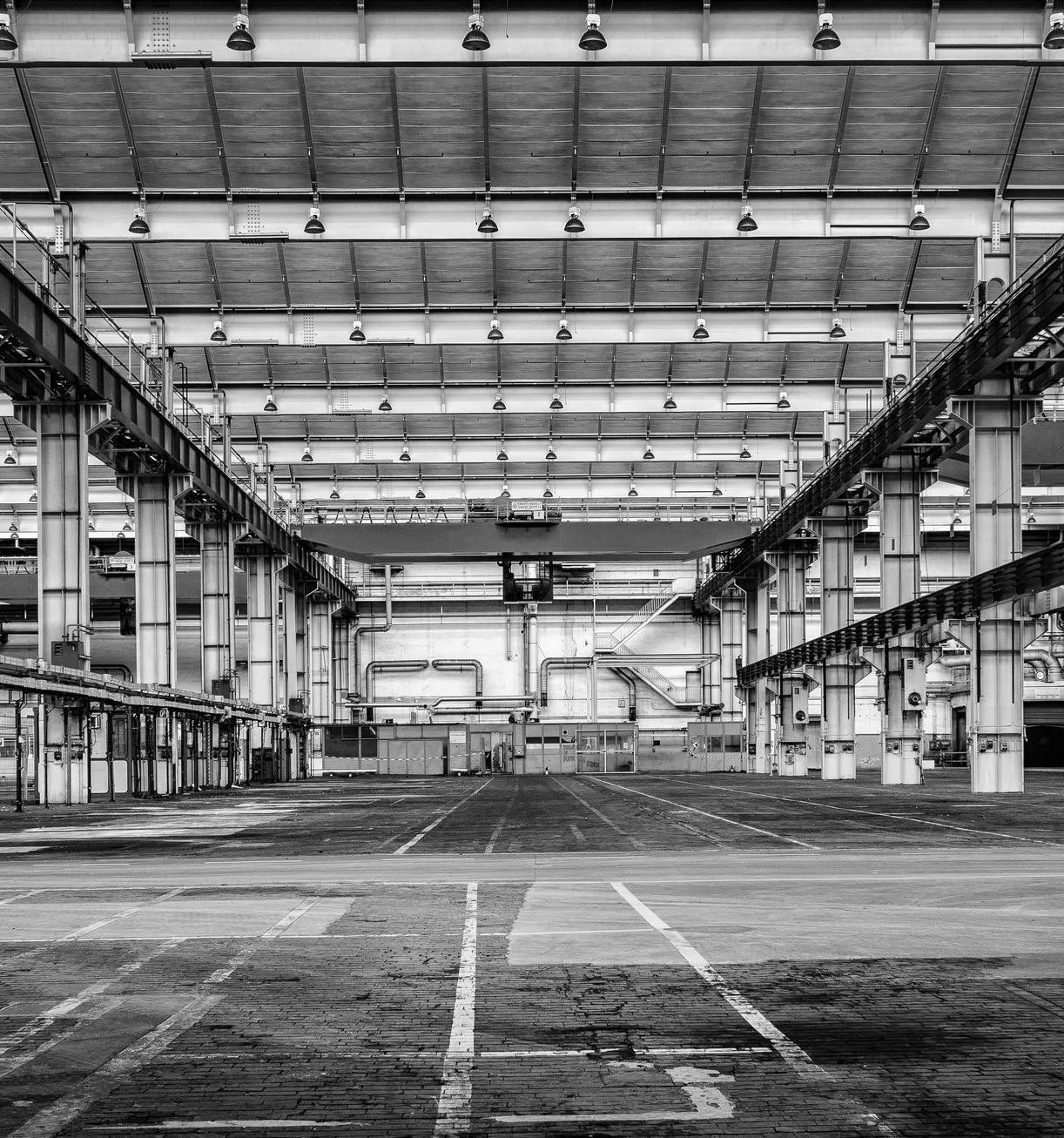 Black and white image of a large industrial interior with overhead crane and support beams.