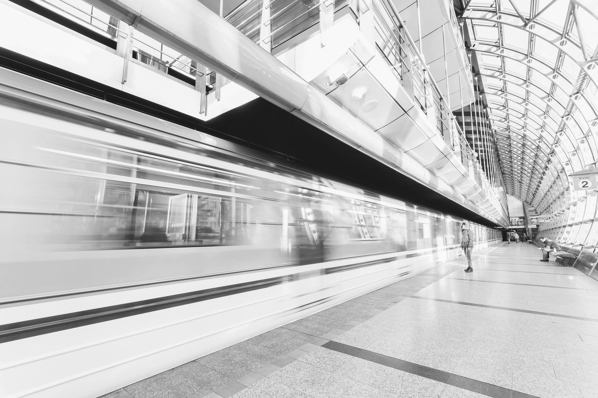Train speeding through modern, glass-covered subway station. Passenger stands on platform.