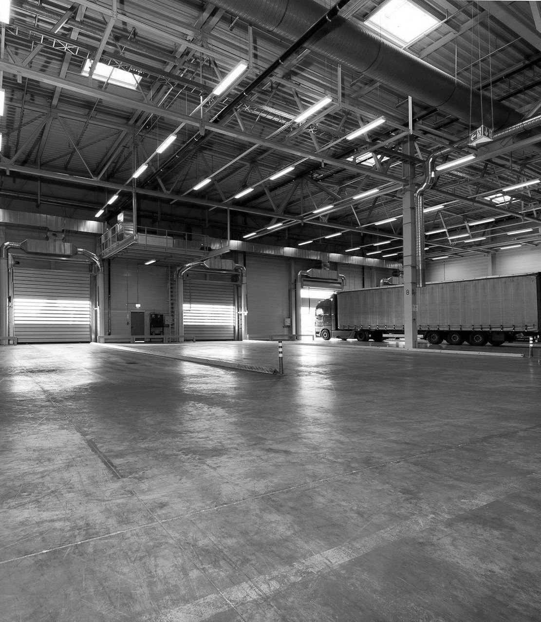 Black and white photo of a warehouse interior with a semi-truck parked at a loading dock.